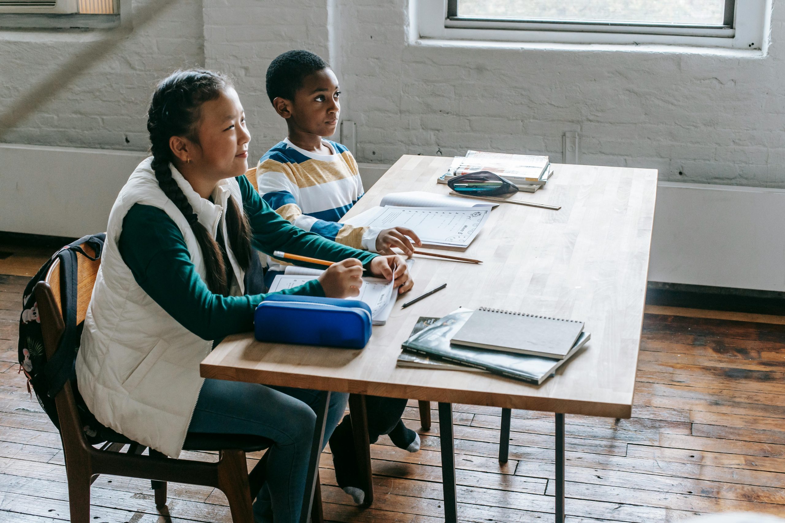 Two diverse children studying together in a well-lit classroom.